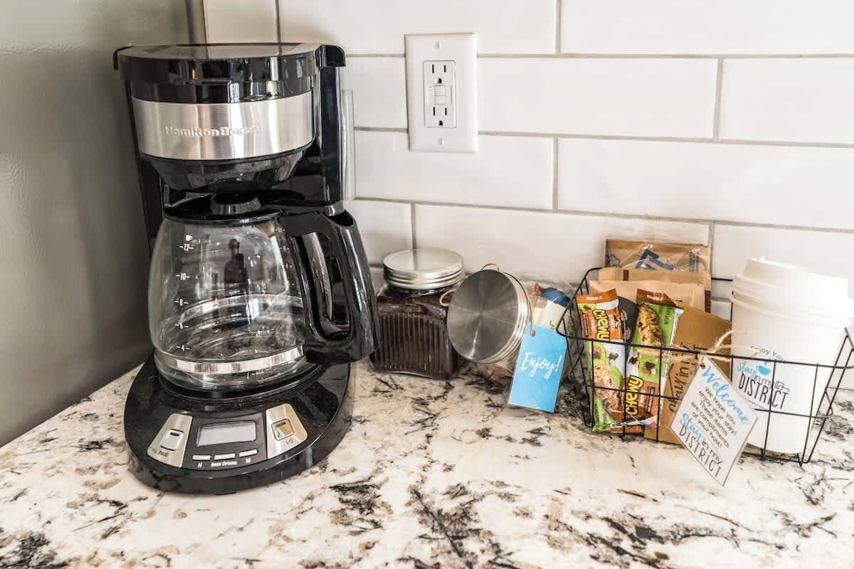 A kitchen with a coffee maker, a countertop, and a basket of snacks.