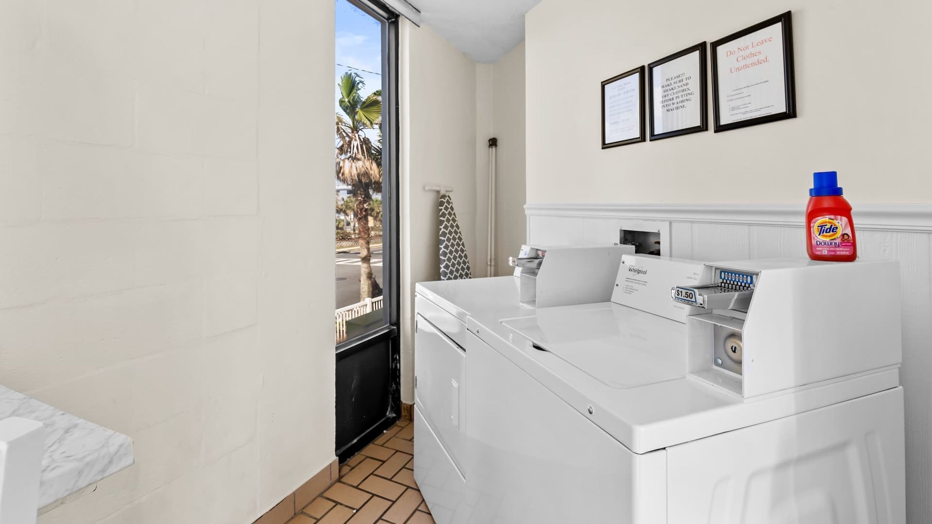 A laundry room with a Whirlpool washer and dryer, a Tide detergent bottle, and three framed notices on the wall.