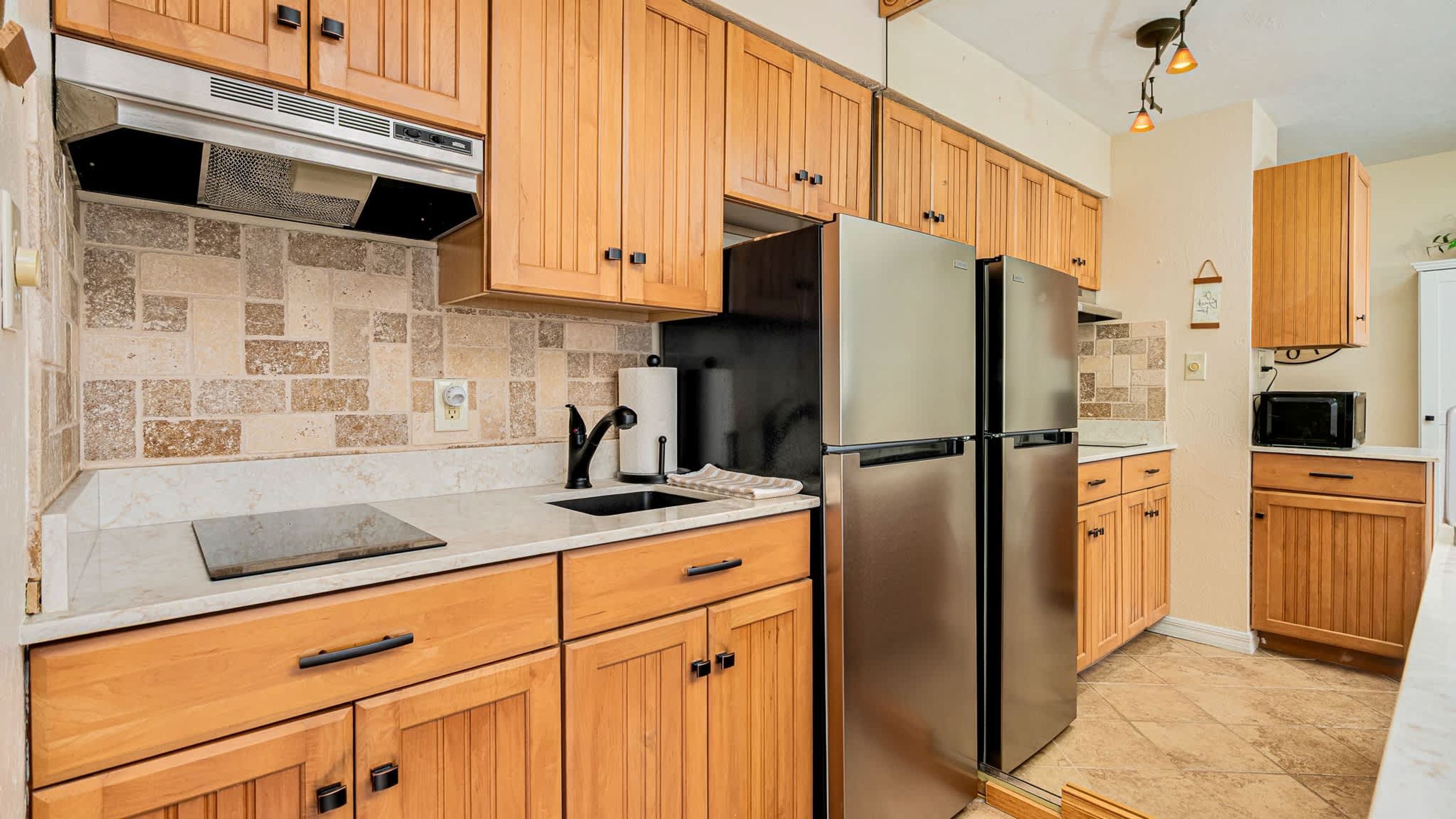 Una cocina moderna con armarios de madera, un refrigerador de acero inoxidable y un protector contra salpicaduras de piedra.