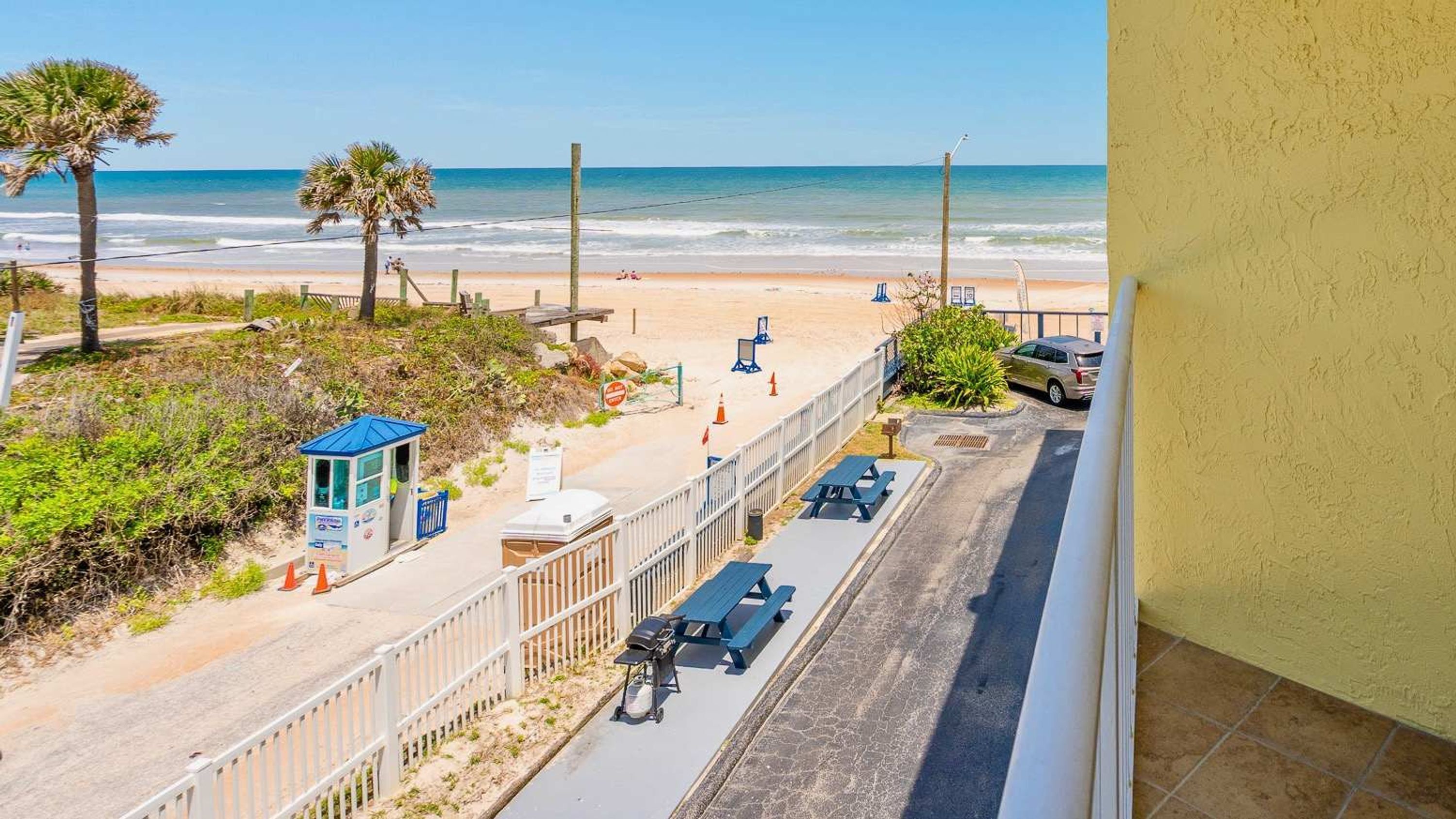 A beach view with a fenced walkway, picnic tables, and a lifeguard station.