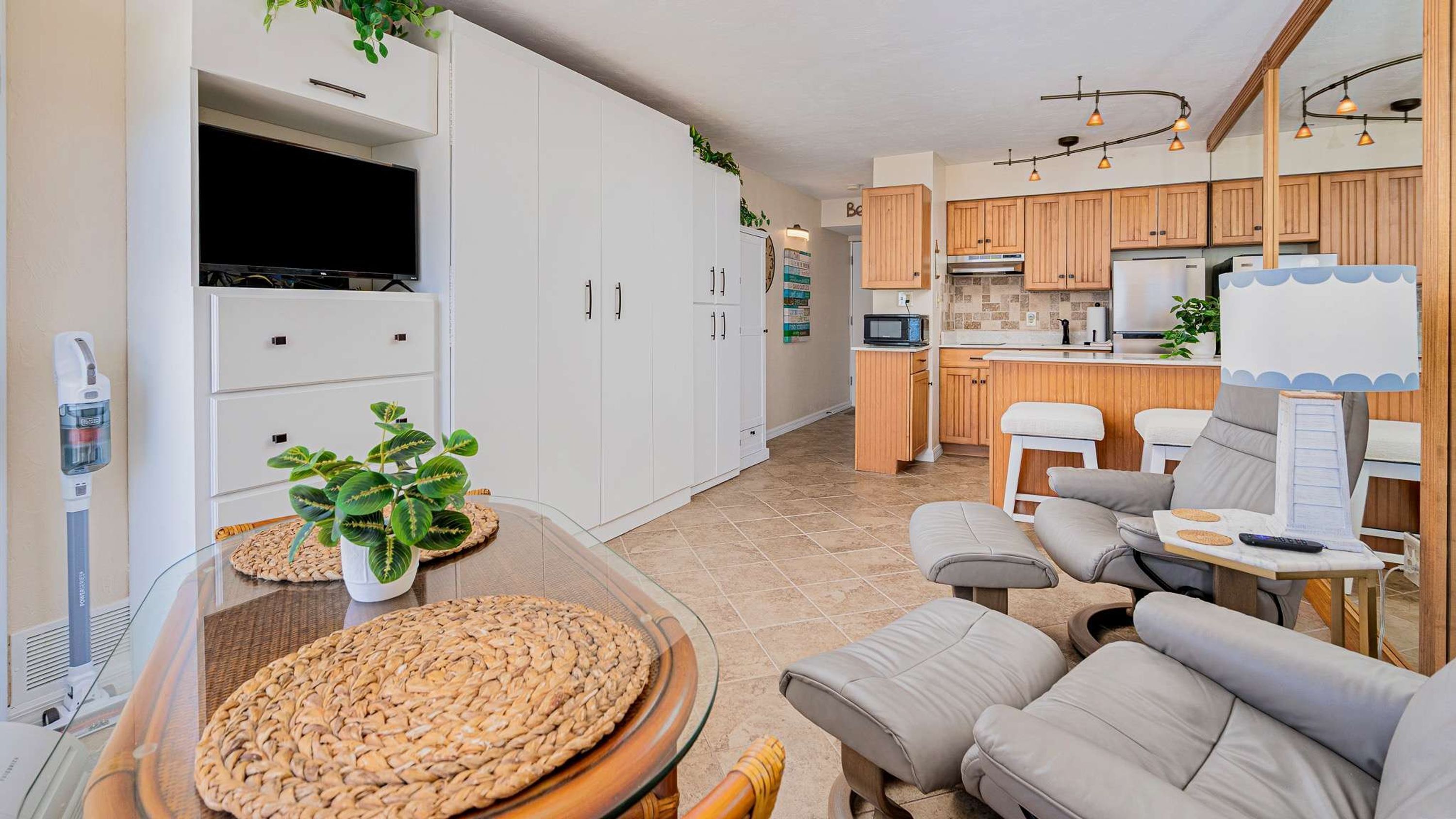 A modern kitchen with wooden cabinets, a central island, and a dining area with a glass table and cushioned seating.