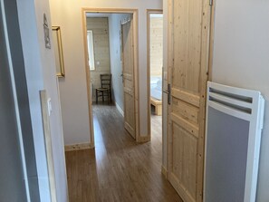 A hallway with wooden flooring, a chair, and a bed in the background. - 2-bedroom chalet Aiguillon R-1G (Le Lioran)