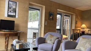 Una habitación acogedora con dos sillones morados, una mesa de madera con un dispensador de pañuelos, un televisor y una ventana con vistas a un paisaje nevado.