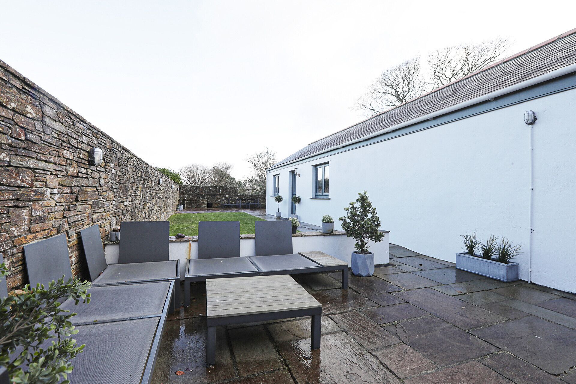 An outdoor patio with a stone wall, a white building, and a table with chairs.