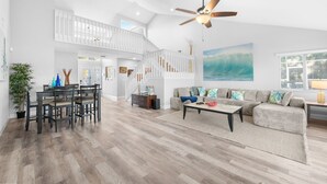 A spacious living area with a high ceiling, a ceiling fan, a staircase, a dining area with a table and chairs, and a large window. - Canal-front Heated Pool Home with Pool Table & Kayaks (Palm Coast)