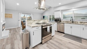 A modern kitchen with white cabinets, a stainless steel range, and a large window with blinds. - Canal-front Heated Pool Home with Pool Table & Kayaks (Palm Coast)