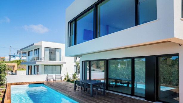 Una casa moderna con piscina, un patio con mesa y sillas, y amplios ventanales de vidrio.