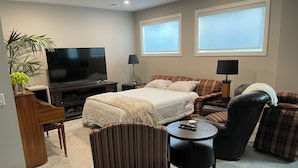 A modern hotel room with a bed, a TV, a desk, a chair, and a sofa. - Two Bedroom Basement Suite (Calgary)