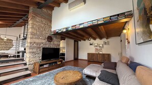 A cozy living room with a stone wall, a flat-screen TV, a wooden coffee table, a sofa, and a bookshelf filled with books. - Apartment in renovated rustic courtyard (Colognola Ai Colli)