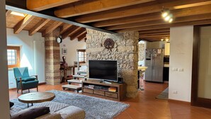 A cozy living room with a stone wall, wooden beams, a TV, and a dining area in the background. - Apartment in renovated rustic courtyard (Colognola Ai Colli)