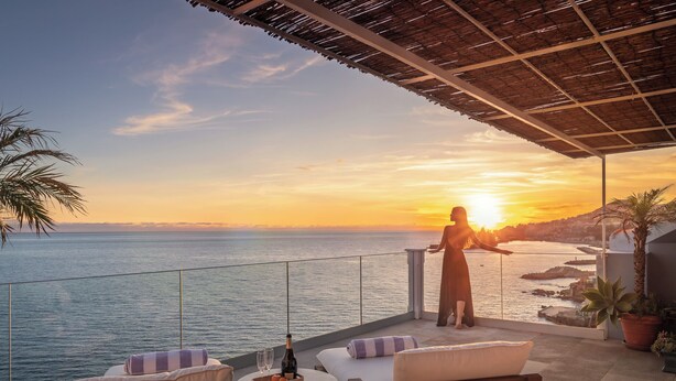 Un balcón con vistas al mar al atardecer, amueblado con un sofá, una mesita y una botella de champán.