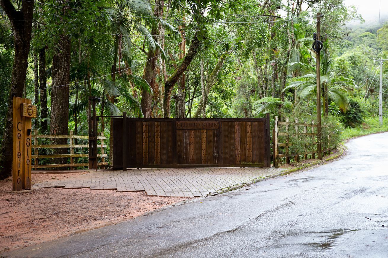 A gated entrance with a wooden fence and a metal gate, surrounded by lush greenery and trees.