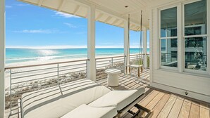 Ein Balkon mit Blick auf den Strand, einer gepolsterten Sitzecke und einem kleinen Tisch.