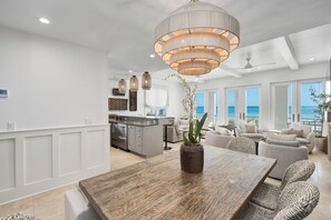 A spacious living area with a wooden dining table, wicker chairs, and a large window overlooking the ocean. - Shared Moments | Private Beach Access | Gulf Front | Hot Tub (Panama City Beach)