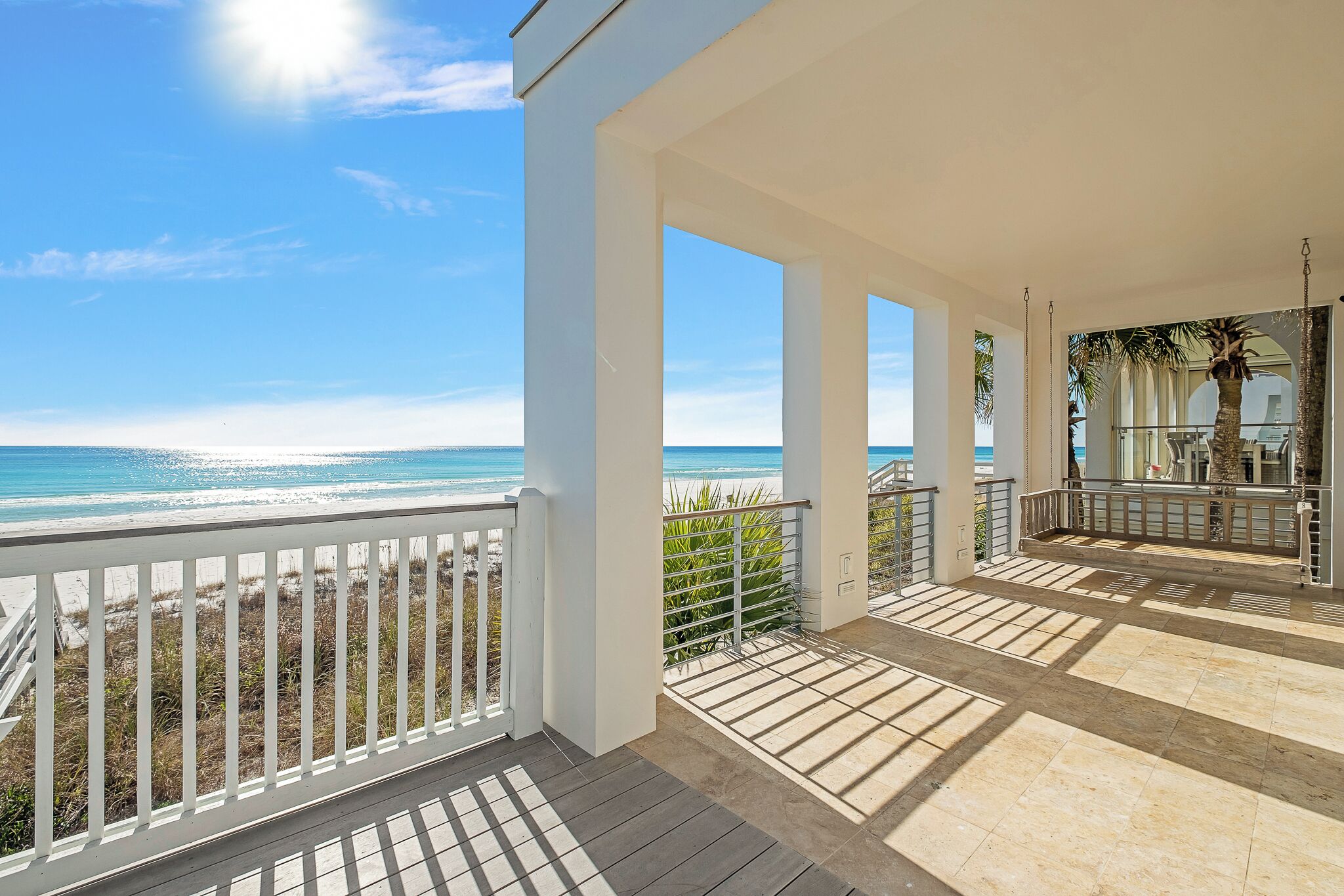 A covered outdoor area with a view of the beach, featuring a wooden deck and a white railing.