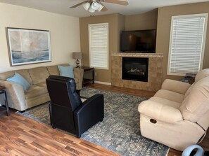 A living room with a fireplace, a television, and a ceiling fan.