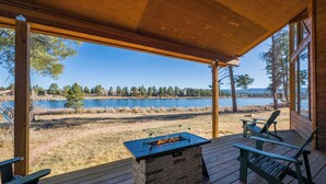Een houten terras met een vuurplaats van steen en twee Adirondack-stoelen, met uitzicht op een meer.