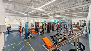 Et træningscenter med diverse træningsmaskiner, en spejlvæg samt loft med synlige bjælker og lys.