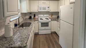 A modern kitchen with white cabinets, a granite countertop, a built-in microwave, a stove, and a refrigerator. - Manning Way (Elon)