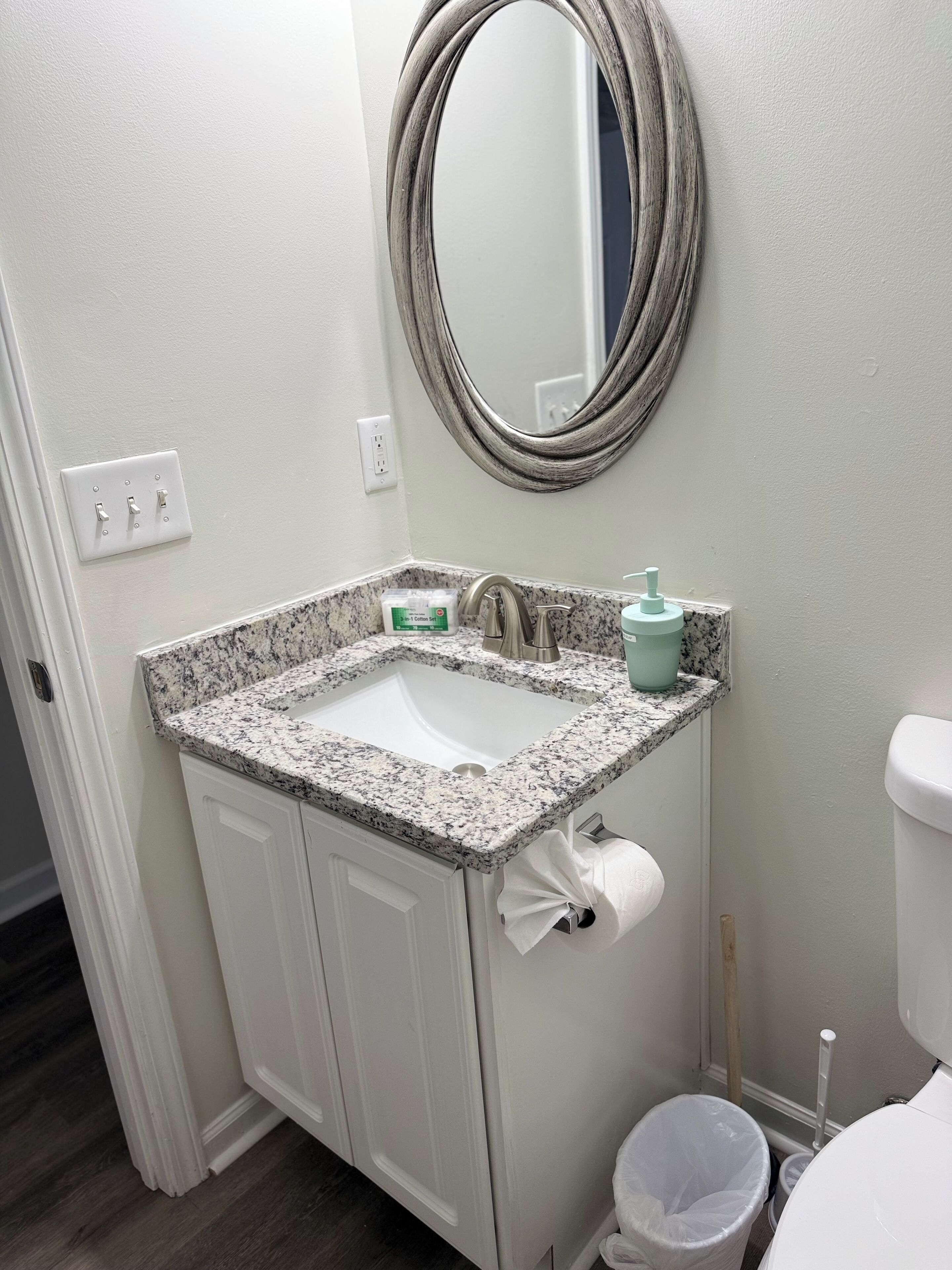 Een badkamer met een wit wastafel, een spiegel, een toilet en een prullenbak.
