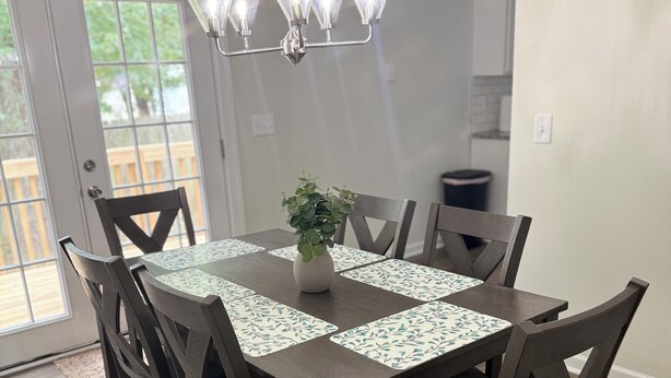 A dining area with a wooden table, dark chairs, a chandelier, and a potted plant. - Manning Way (Elon)