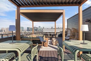 Une terrasse sur le toit, aménagée avec des espaces salon, une pergola et offrant une vue sur le panorama urbain.