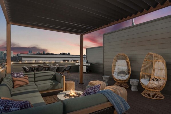Une terrasse sur le toit avec un canapé vert, des fauteuils en osier, un foyer et une vue imprenable sur les toits de la ville.