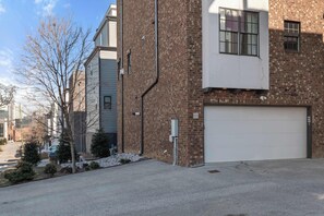 Un bâtiment en briques de deux étages, avec une porte de garage blanche, un petit arbre devant et un ciel dégagé.