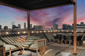 Une terrasse sur le toit offrant une vue panoramique sur la ville, avec des sièges en plein air et des guirlandes lumineuses.