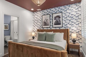 Une chambre à coucher avec un lit en bois, deux oreillers, une table de chevet avec une lampe et un mur recouvert d’un papier peint à motifs de chevaux.