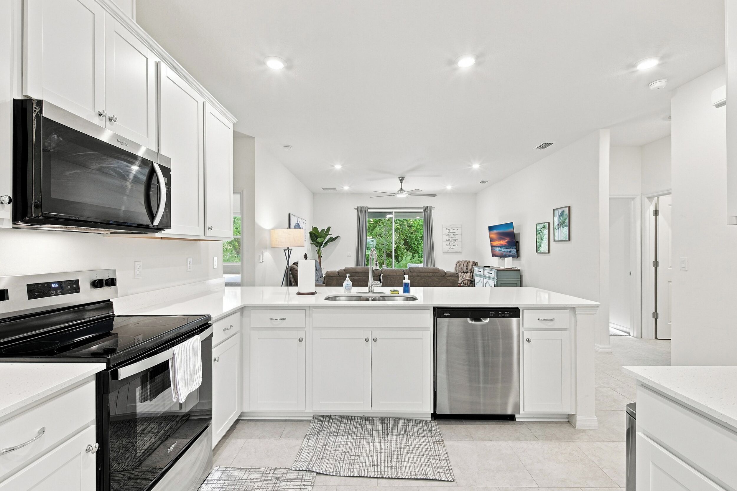 A modern kitchen with white cabinetry, a built-in microwave, a stainless steel dishwasher, and a large island with a sink.