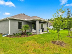 A residential house with a covered patio, a lawn, and a small tree.