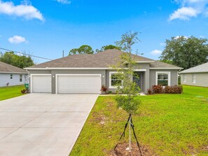 A single-story house with a garage, a small lawn, and a tree. - Sebastian Serenity - 4BR/2BA home near beaches (Sebastian)