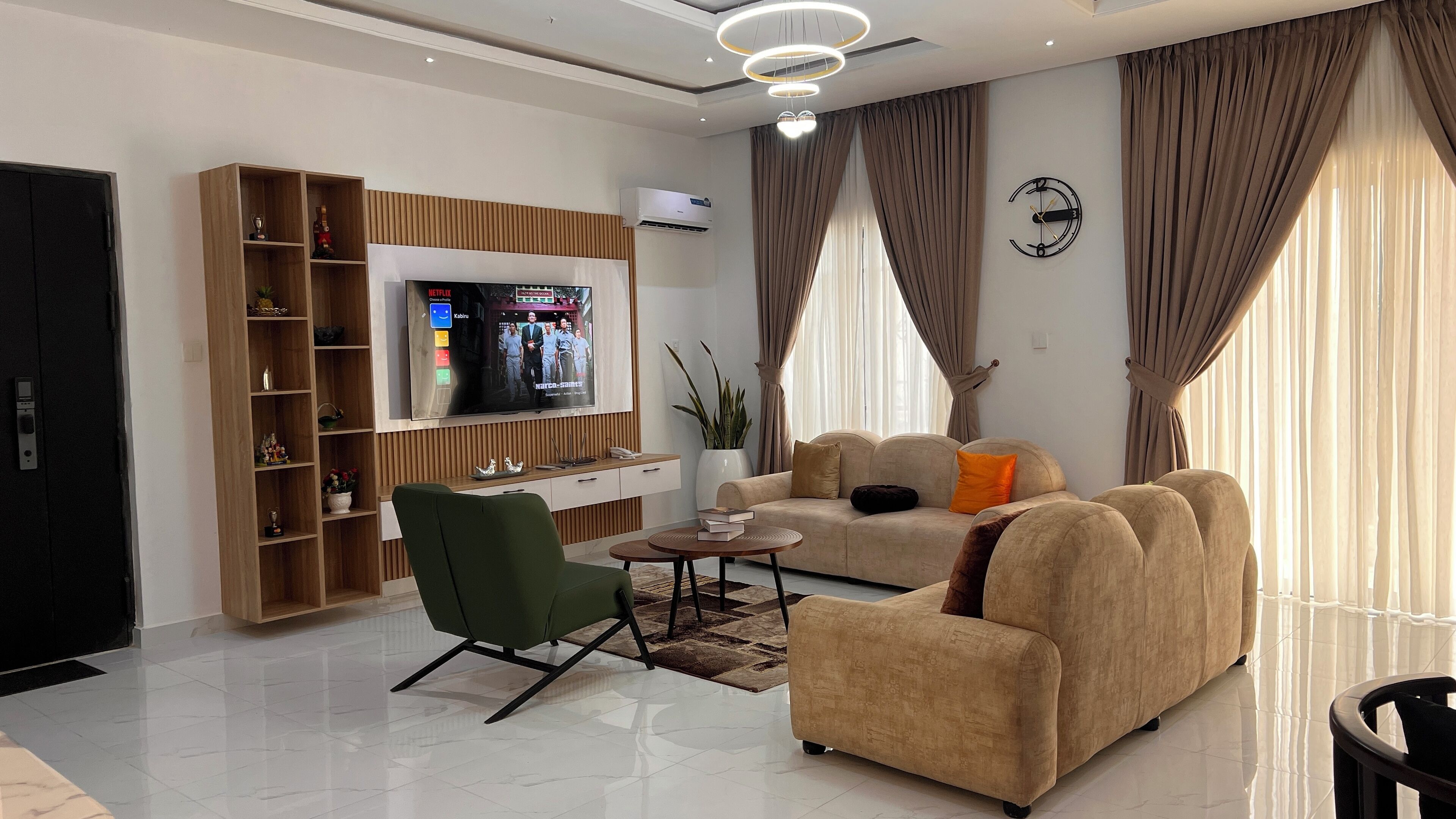 A modern living room with a flat-screen TV, a green armchair, a beige sofa, and a coffee table.