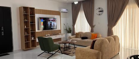 Una sala moderna con una televisión de pantalla plana, un sillón verde, un sofá beige y una mesita de centro.