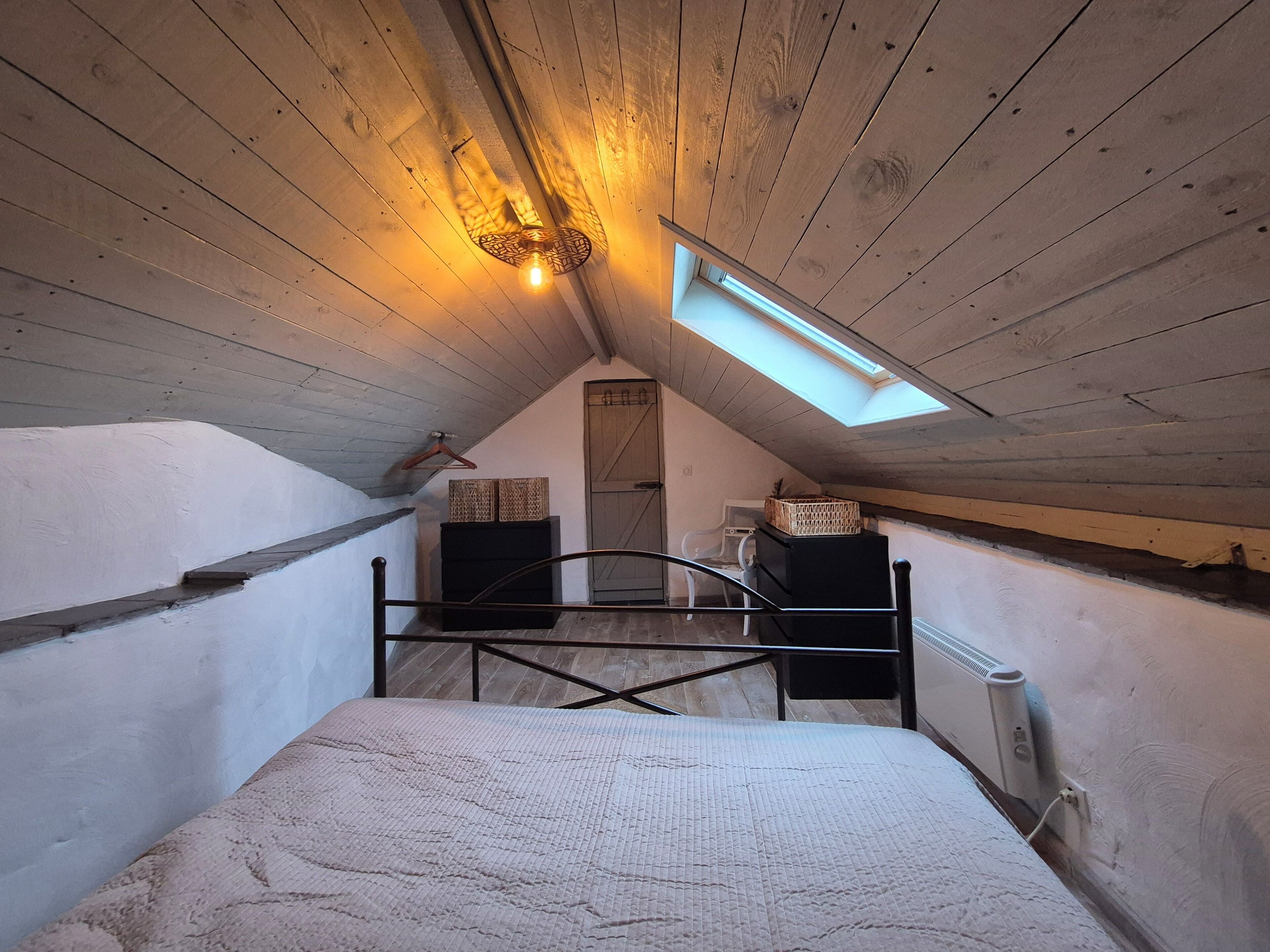Een slaapkamer met een schuine plafond, dakraam, bed, radiator en een dressoir.