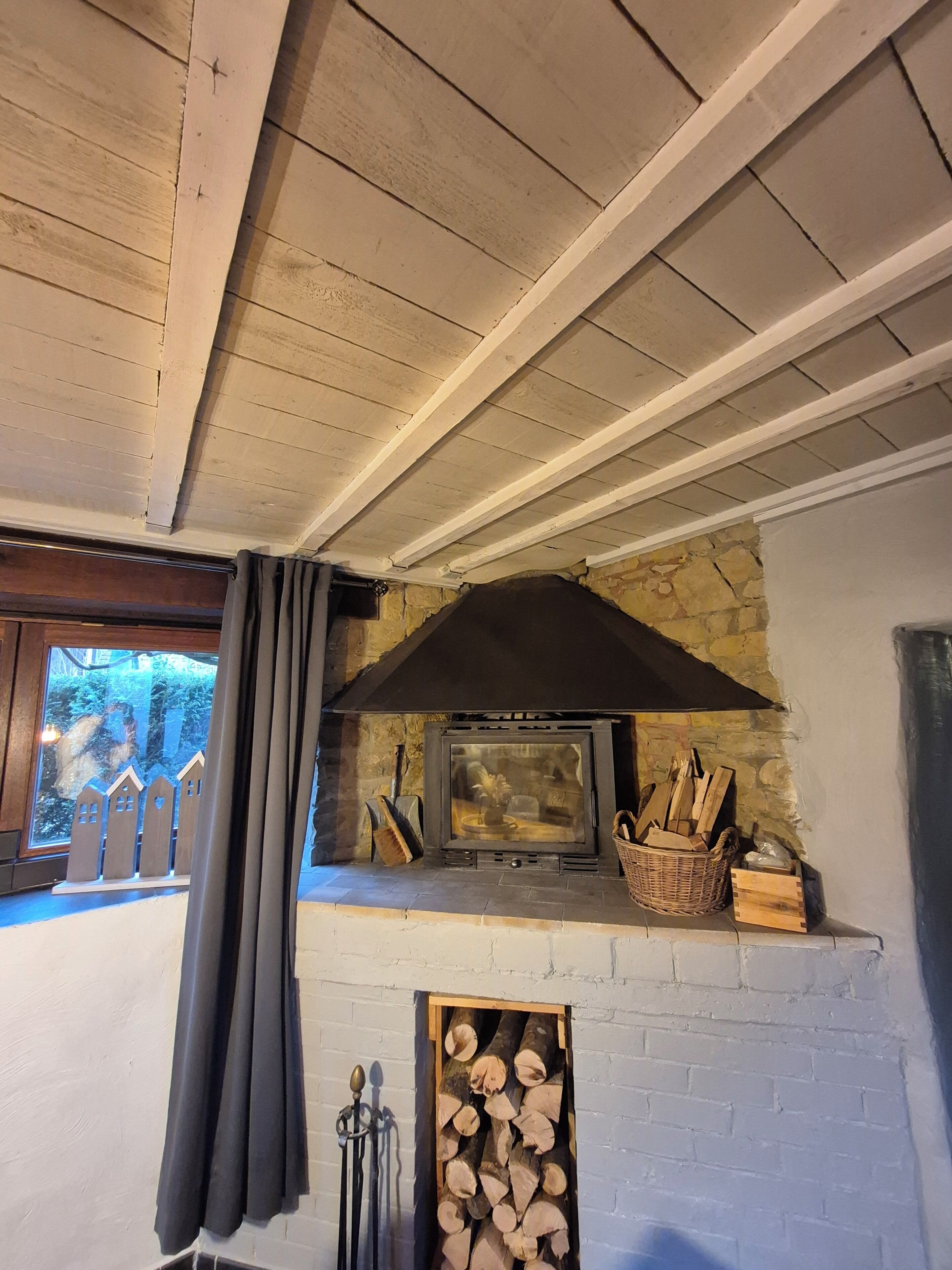 Un interior rústico con chimenea de piedra, techo de madera y vista a una valla de madera desde el exterior.