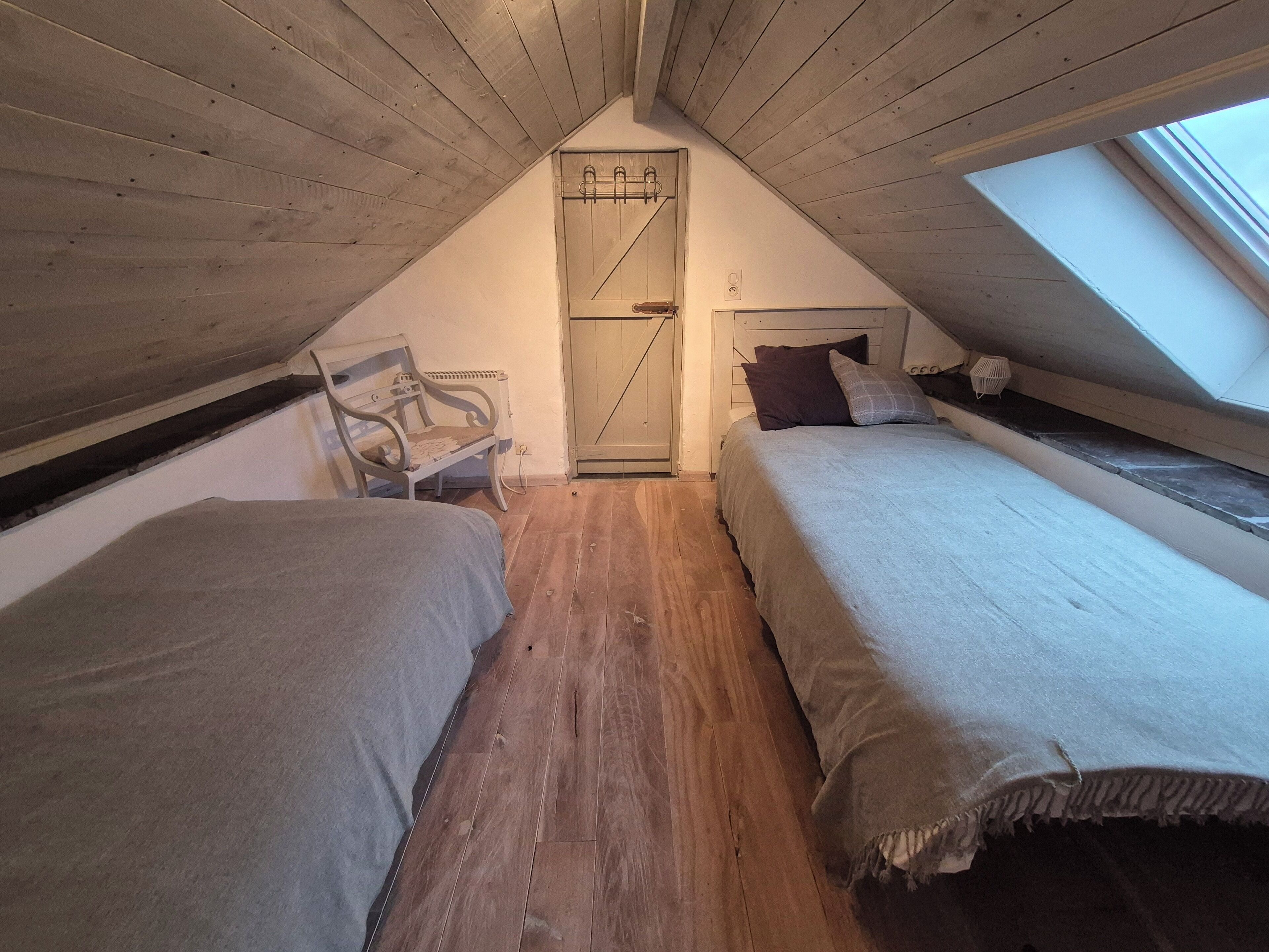 Ein kleines Schlafzimmer im Dachgeschoss mit zwei Betten, einer Bank und einem Oberlicht.