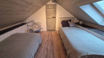 Ein kleines Schlafzimmer im Dachgeschoss mit zwei Betten, einer Bank und einem Oberlicht.