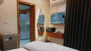 A hotel room with a bed, a mirror, a television, and a minibar.