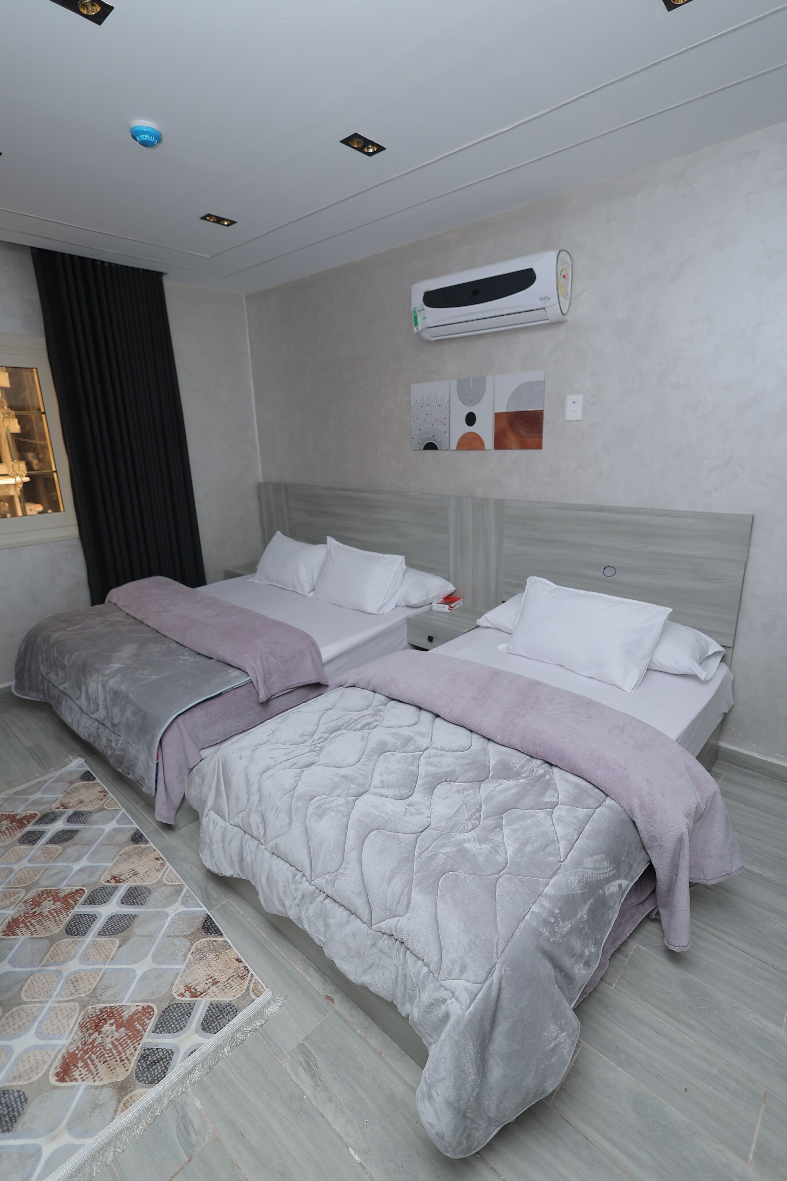 Une chambre d’hôtel moderne avec deux lits, une grande fenêtre avec des rideaux, un appareil de climatisation et un tapis à motifs.