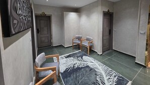 A spacious hallway with a modern design, featuring a patterned rug, two wooden chairs, and a door labeled "ROOM 1".