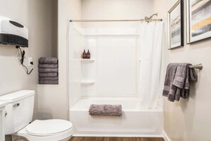 A bathroom with a toilet, a bathtub, a shower curtain, and towels. - #StayinMyDistrict 2BR Walk to Downtown Nampa (Nampa)