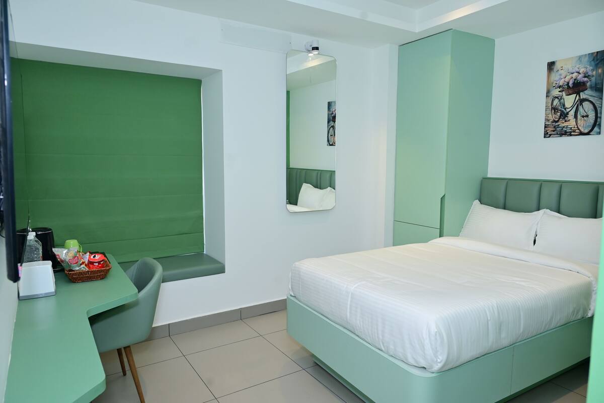 A room with a bed, a desk, a chair, a mirror, and a wall-mounted artwork.