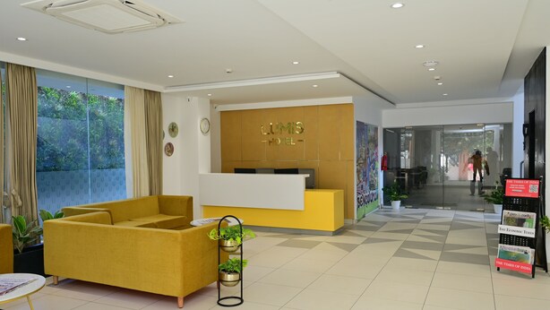 A hotel reception area with a yellow reception desk, a large window with curtains, and a reception counter. - Lumis Hotel (Bengaluru)