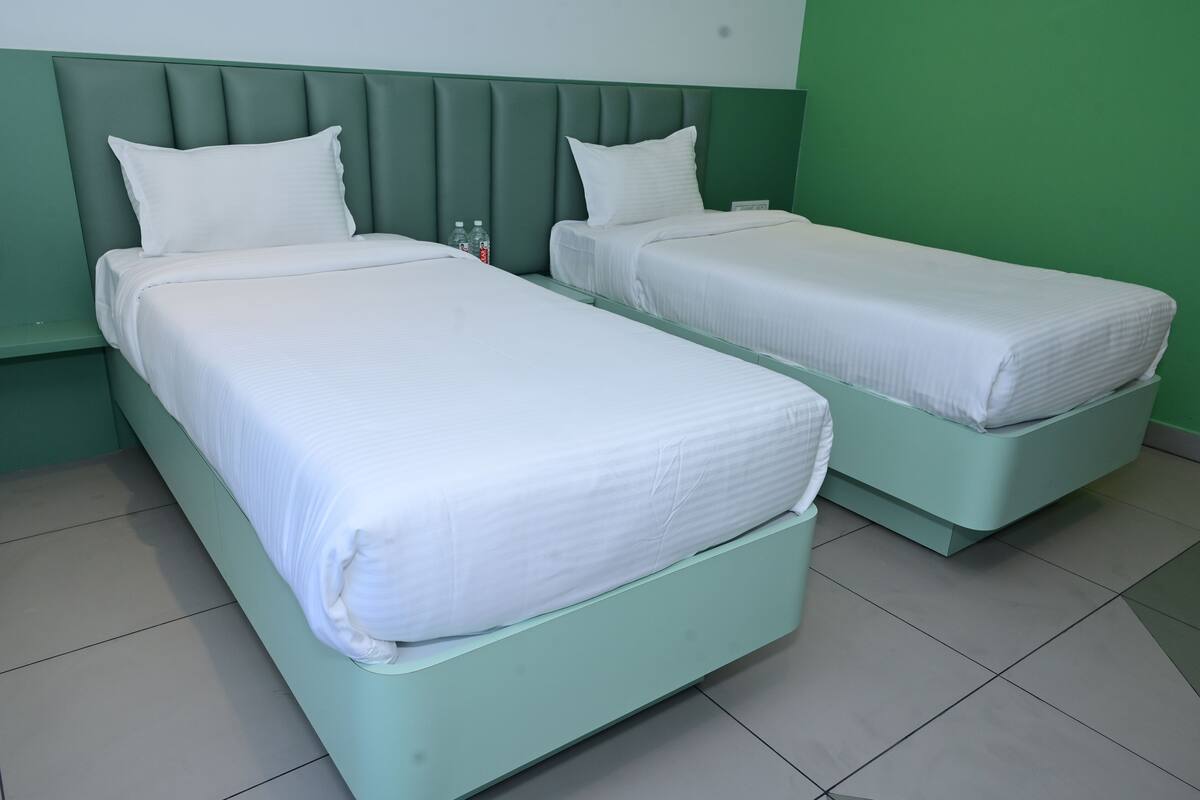 Two twin beds with green headboards and white bedding in a room with green walls and tiled flooring.