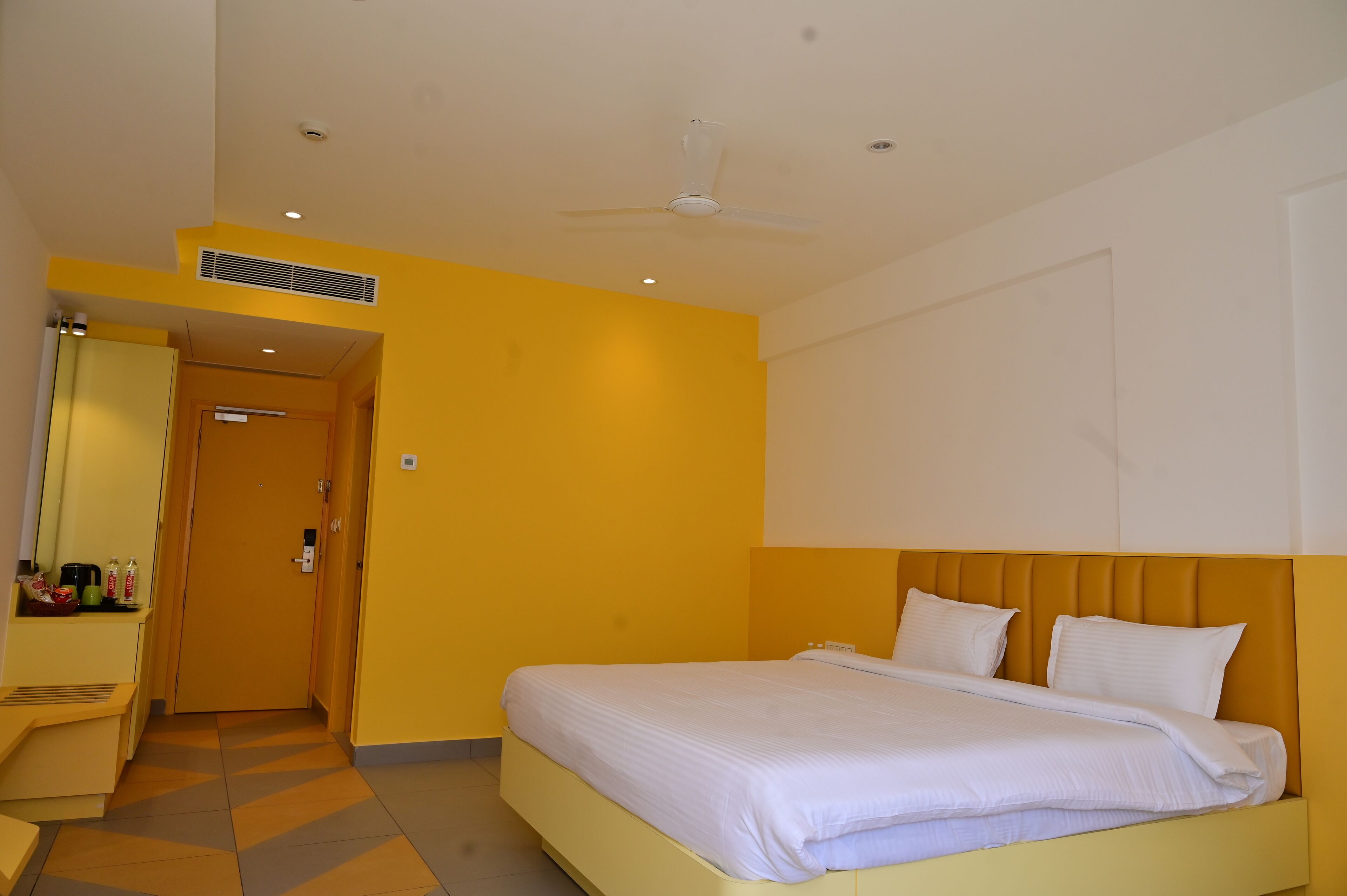 A hotel room with a bed, a desk, a mirror, and a door.
