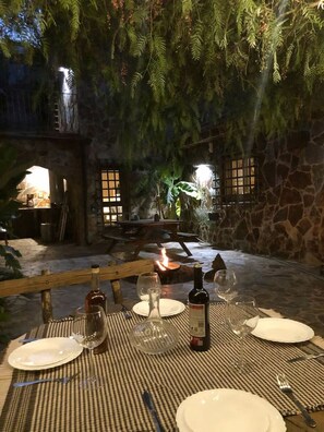 Un espace de restauration en plein air avec des tables pour deux, entouré de murs en pierre et de verdure.