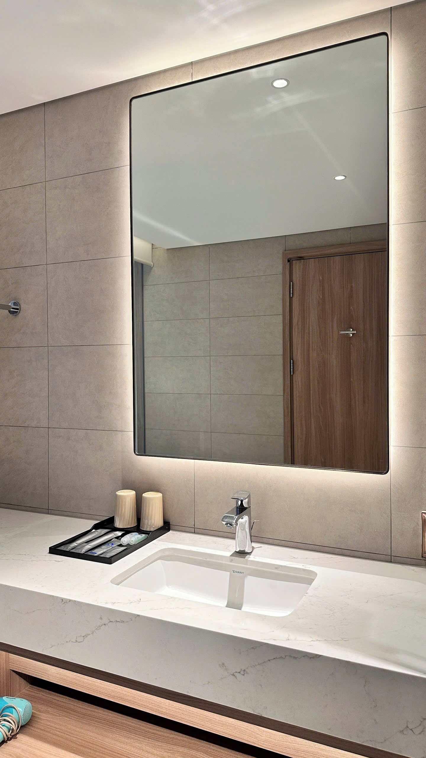 A modern bathroom with a large mirror, a sink with a faucet, and a wooden cabinet.