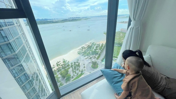 A high-rise room with a large window overlooking a beach and water. - A La carte Ha Long Apartment Sea View  (Bai Chay)